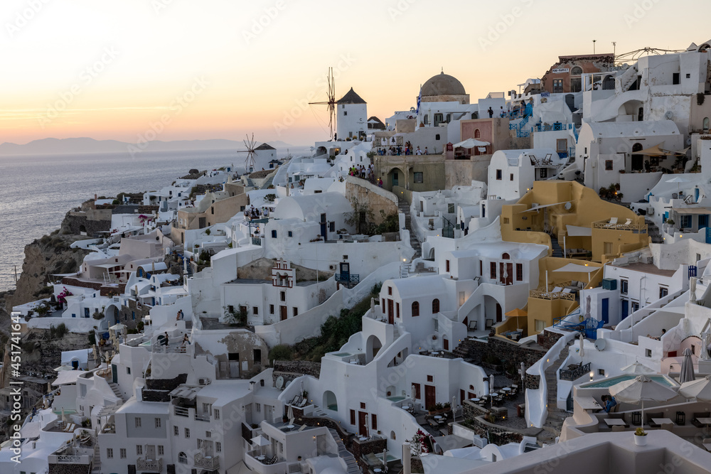 Whitewashed houses and windmills in Oia in warm rays of sunset on Santorini island. Greece