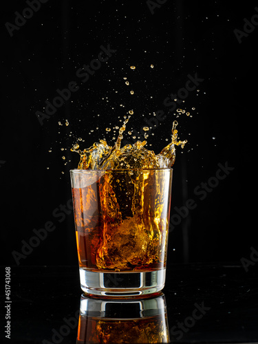 splash in glass with whiskey with ice on black background