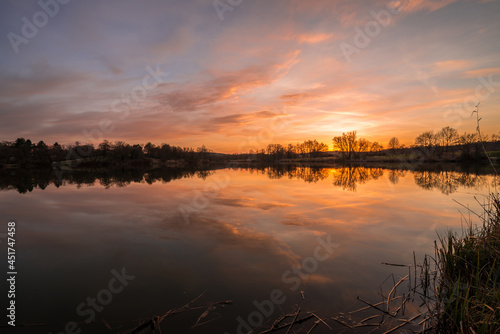 Landschaft und Sonnenuntergang am Ufer im Westpark Donaupark in Regensburg mit Spiegelung des Himmels in dem glatten See mit wunderschönen dramatisch Farben Farbenspiel mit Wolken, Deutschland