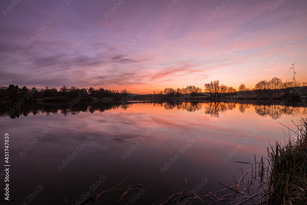 Landschaft und Sonnenuntergang am Ufer im Westpark Donaupark in Regensburg mit Spiegelung des Himmels in dem glatten See mit wunderschönen dramatisch Farben Farbenspiel mit Wolken, Deutschland