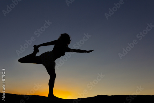 Silhouette of woman practicing yoga at sunset on a rock in nature. Backlight. Copy space.