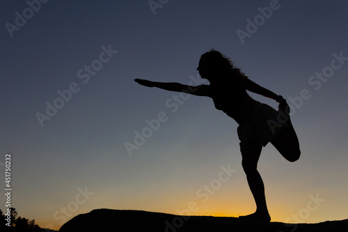 Silhouette of woman practicing yoga at sunset on a rock in nature. Backlight. Copy space.