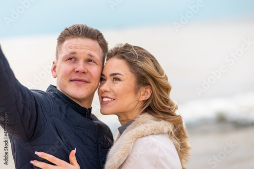 Beautiful young happy woman hugging cuddle young boyfriend while taking selfie photo on sunny beach.Close up.