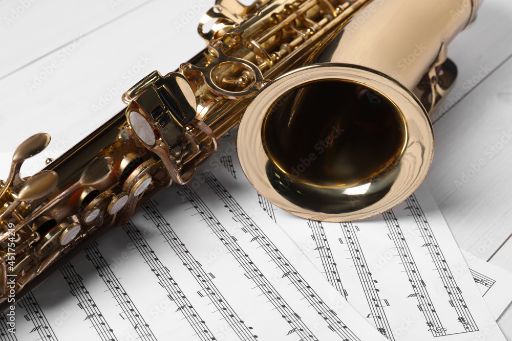 Naklejka premium Beautiful saxophone and note sheets on white wooden background, closeup