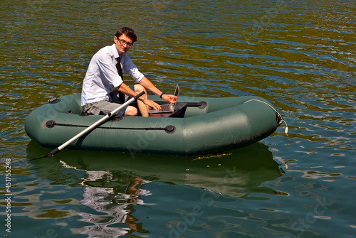 A man in a white shirt on an inflatable boat. Businessman with laptop resting on the lake. The concept of remote work, leisure and freelance.