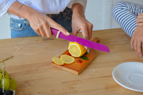 Close-up woman hands cut lemon with sharp knife in kitchen