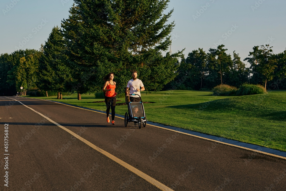 Active family running. Young family with their kid in a jogging stroller during jogging in a public park