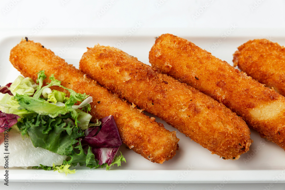 Fried cheese sticks with fresh green salad leaves. Appetizing snack. Close-up. White background.