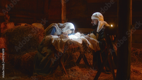 Fotografie, Tablou Mary and Joseph caressing baby Jesus in illuminated manger
