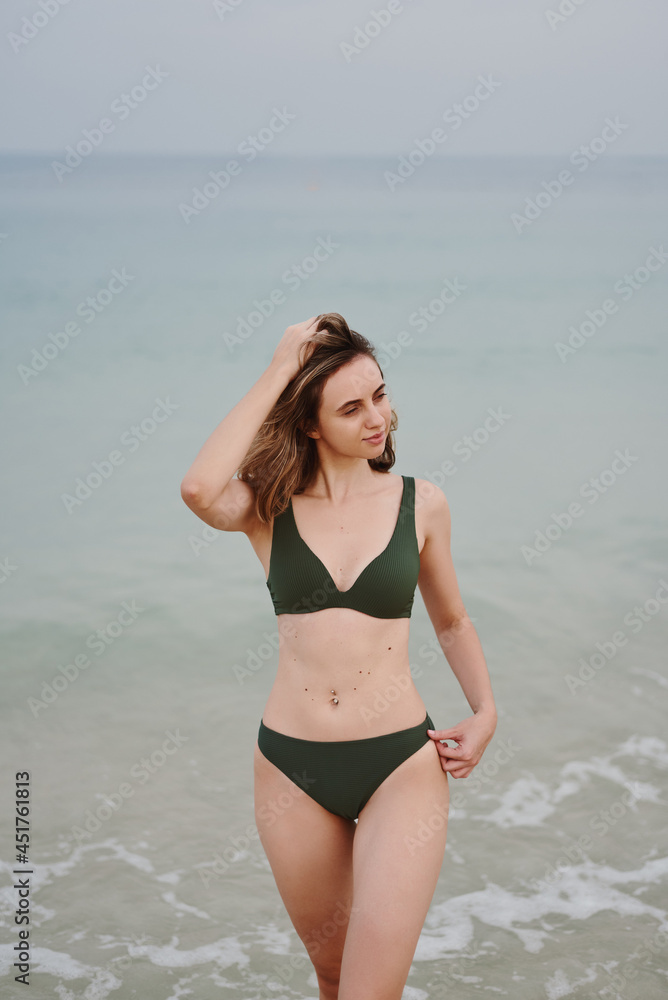 Young woman wearing khaki bikini standing at the beach near water. Travel and vacation