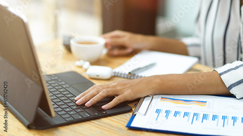 business woman typing on portable tablet, holding a cup of tea, financial report on working desk