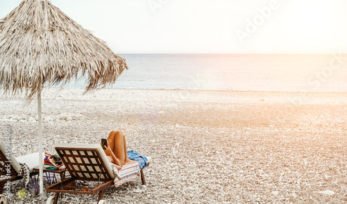 Fototapeta Naklejka Na Ścianę i Meble -  Beach with a woman resting in a sun lounger. Rest and relaxation on the sea beach under the sun.