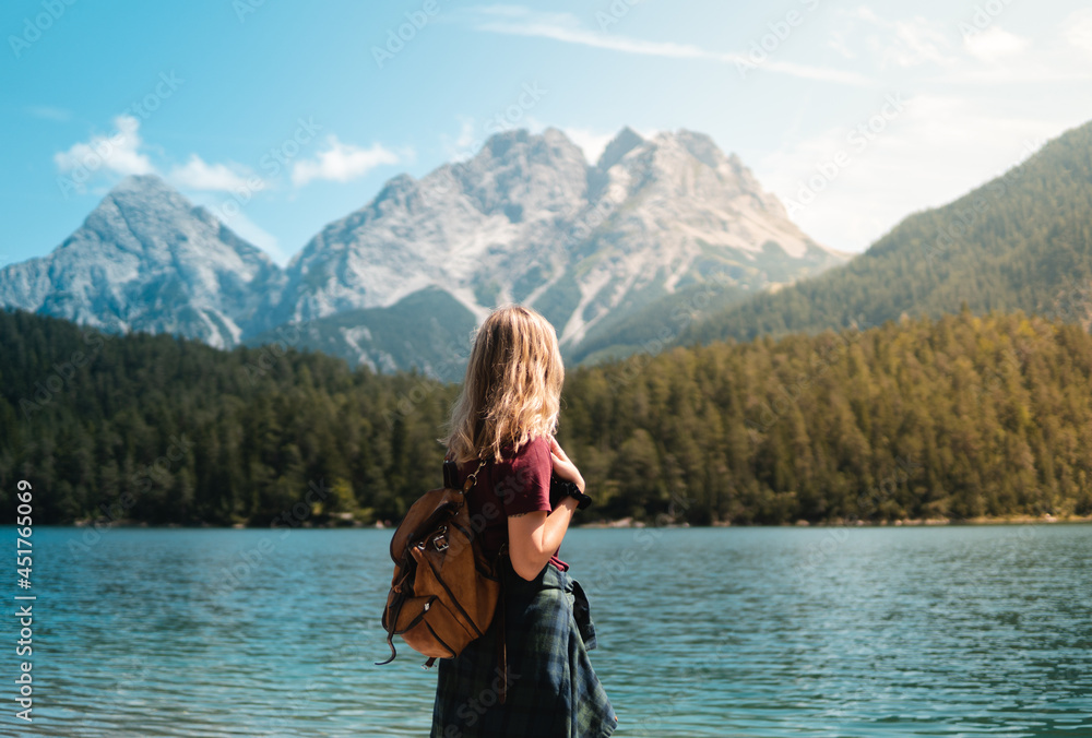 Young blonde woman stops to contemplate Blindsee lake with the Biberwierer Scharte in the background, alpine image in Austria, hiking and happiness in the alps. Backpacking and hiking in nature.