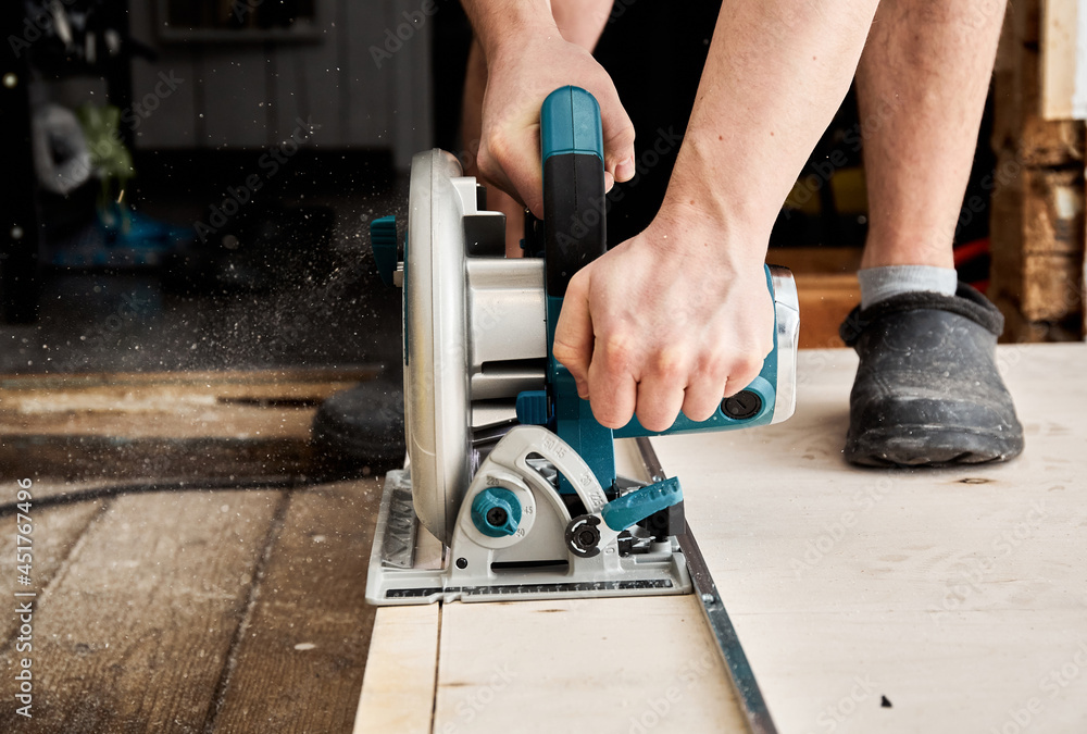 Sawing plywood by circular saw. Home repair. Hand tool. Man hold equipment. Building process. Woodworking. Safety engineering. Without gloves. Copy space. Indoor. Cutting material. Rental instrument Sawing plywood by circular saw. Home repair. Hand tool. Man hold equipment. Building process. Woodworking. Safety engineering. Without gloves. Copy space. Indoor. Cutting material. Rental instrument