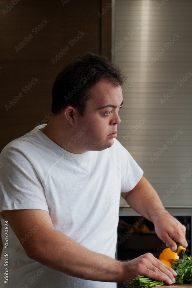 Young man with Down Syndrome cutting fresh vegetables in the kitchen Young man with Down Syndrome cutting fresh vegetables in the kitchen
