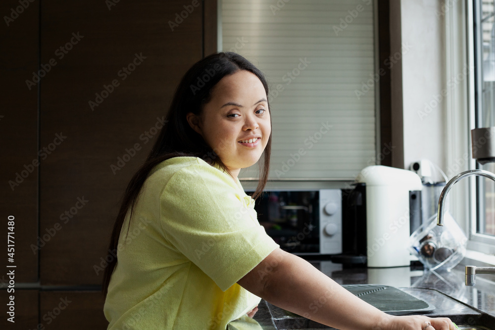 Young biracial woman with Down Syndrome cleaning the kitchen and smiling