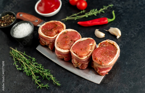 raw pork tenderloin medallions wrapped in bacon on a stone background	