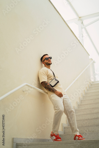 Chico joven atletico tatuado posando en escaleras con tono cromatico crema