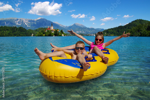 Boy and girl on inflatable float in lake. Little children floating in yellow raft on surface water. © Alekss