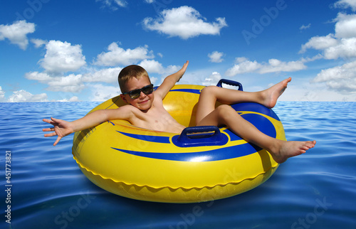 Little boy on inflatable ring in blue sea water surface . © Alekss