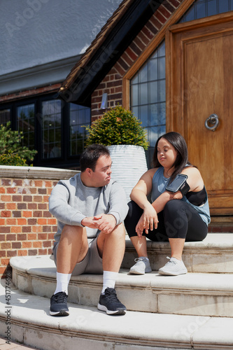 Young biracial couple with Down Syndrome in active wear and wearable tech sitting on steps