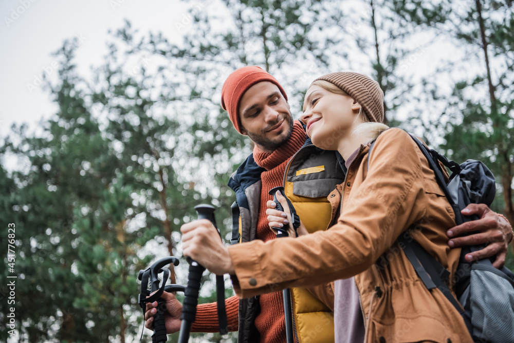 happy man hugging girlfriend with hiking sticks in forest happy man hugging girlfriend with hiking sticks in forest