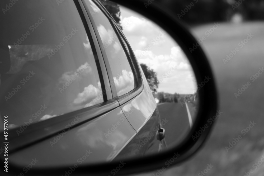 Road and sky with clouds. Rear view in car mirror. Road travel concept. Black and white photo