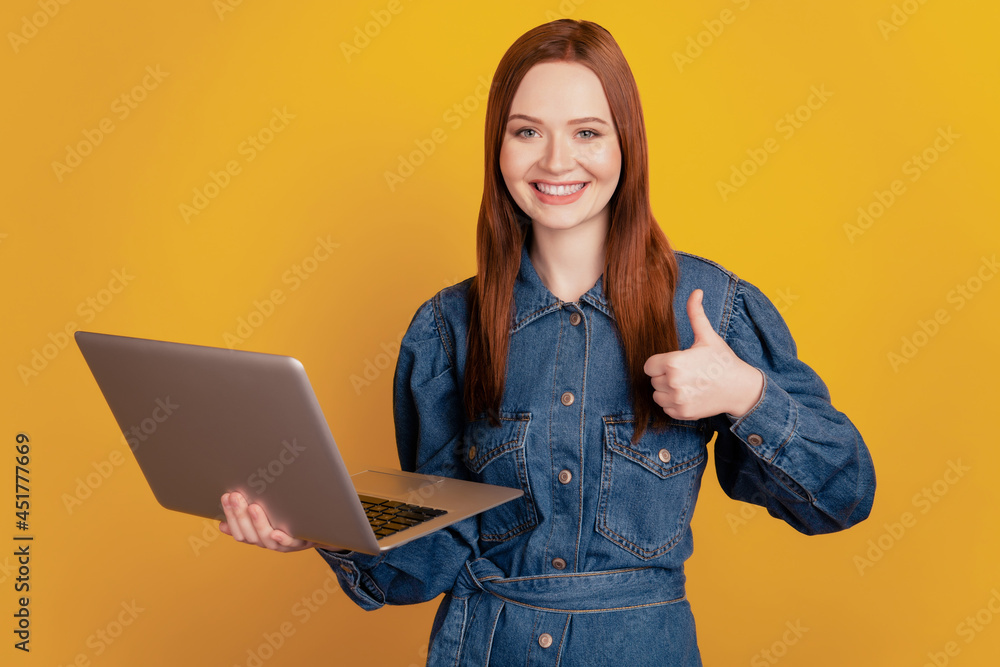 Portrait of charming reliable lady hold laptop raise thumb up approve new gadget model on yellow background Portrait of charming reliable lady hold laptop raise thumb up approve new gadget model on yellow background
