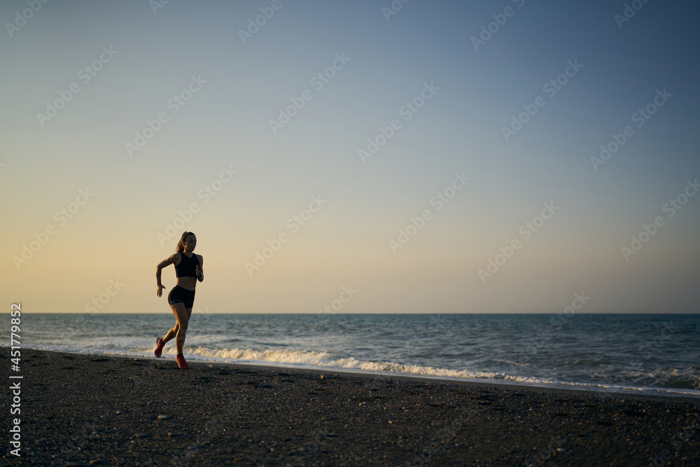 young professional female athlete running on a sunrise in the beach