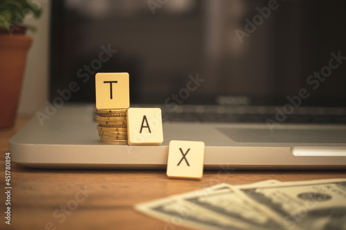 TAX text on business desk with laptop and dollar bills. Taxation, banking revenue concept background