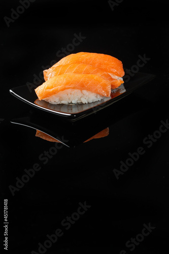 Sushi roll with reflection on a black background. A restaurant with Japanese cuisine. Women's hands holding sushi rolls.