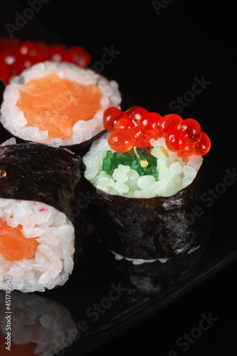 Sushi roll with reflection on a black background. Japanese kitchen and restaurant. Dark sushi rolls with red salmon caviar.