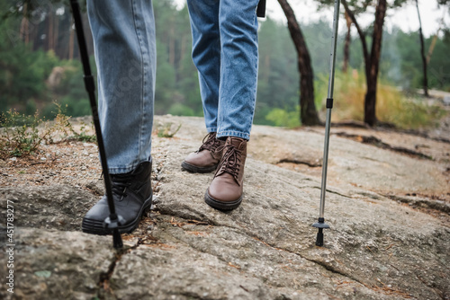 cropped view of young couple standing with hiking sticks on rocky ground