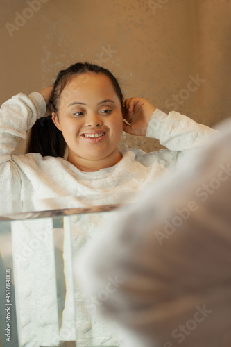 Young biracial woman with Down Syndrome tying her hair in the bathroom and smiling