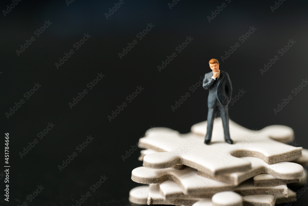 Miniature people Group Business man mini figures standing thinking on Jigsaw Puzzle black background with copy space using as thinking business plan and how to solve problem Strategy Planning concepts
