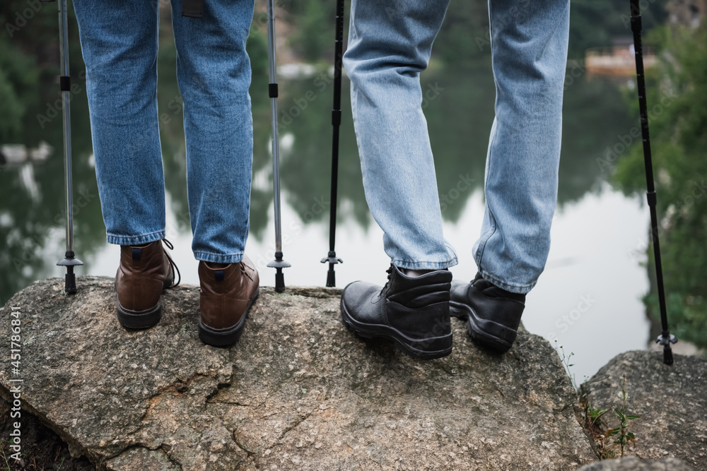 partial view of young couple standing with hiking sticks on rock partial view of young couple standing with hiking sticks on rock