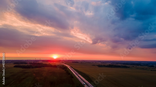Aerial view of highway on red sunset. Landscape with road near countryside fields. Beautiful winding road leading through rural countryside with evening sunlight. Dramatic sky background. © kalyanby