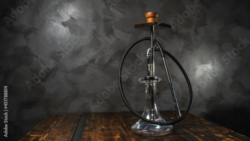 Modern hookah with glass bowl on wooden table. Gray wall background. Lounge concept.