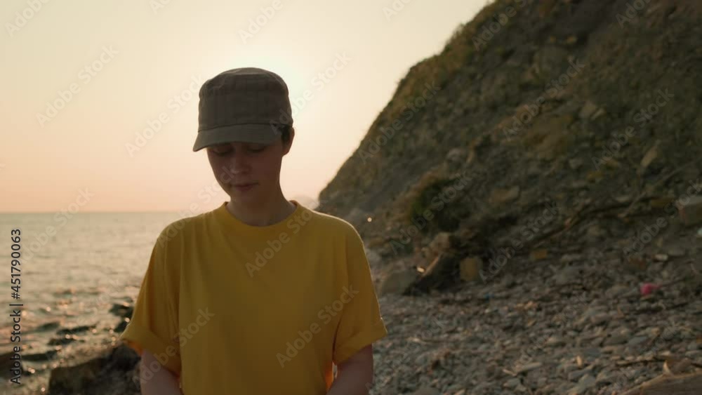Cleaning the ocean shore. A female volunteer walks along a dirty beach, wearing rubber gloves. Hands close-up. The concept of Earth Day. Cleaning the ocean shore. A female volunteer walks along a dirty beach, wearing rubber gloves. Hands close-up. The concept of Earth Day.