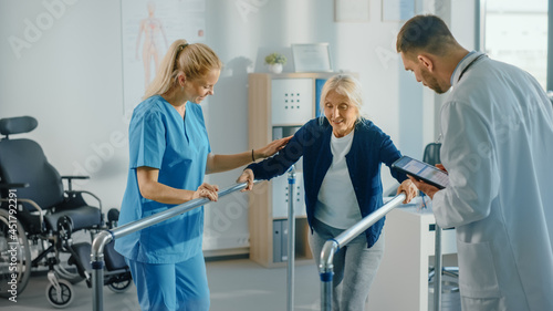 Hospital Physical Therapy: Portrait of Strong Senior Female Patient with Injury Successfully Walks Holding Parallel Bars. Physiotherapist, Rehabilitation Doctor, Help, Assist Disabled Patient