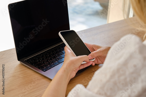 The girl sits at a table in front of a laptop and uses a smartphone for work. Remote work from home. Office desk with laptop and smartphone. Business background. Home office