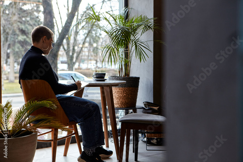 Young girl with short hair and nose piercing sits in a cafe and work at a tablet. The concept of freelancing and remote work.