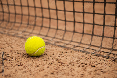 A new tennis ball is lying on a sand court near the net. © Илья Мышенков