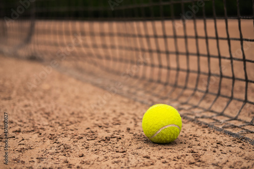 A new tennis ball is lying on a sand court near the net. © Илья Мышенков
