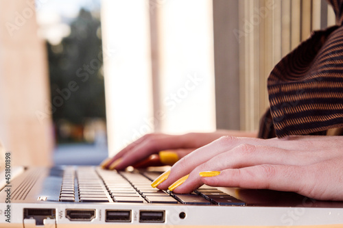 Close-up of young woman hands with yellow painted nails working in laptop