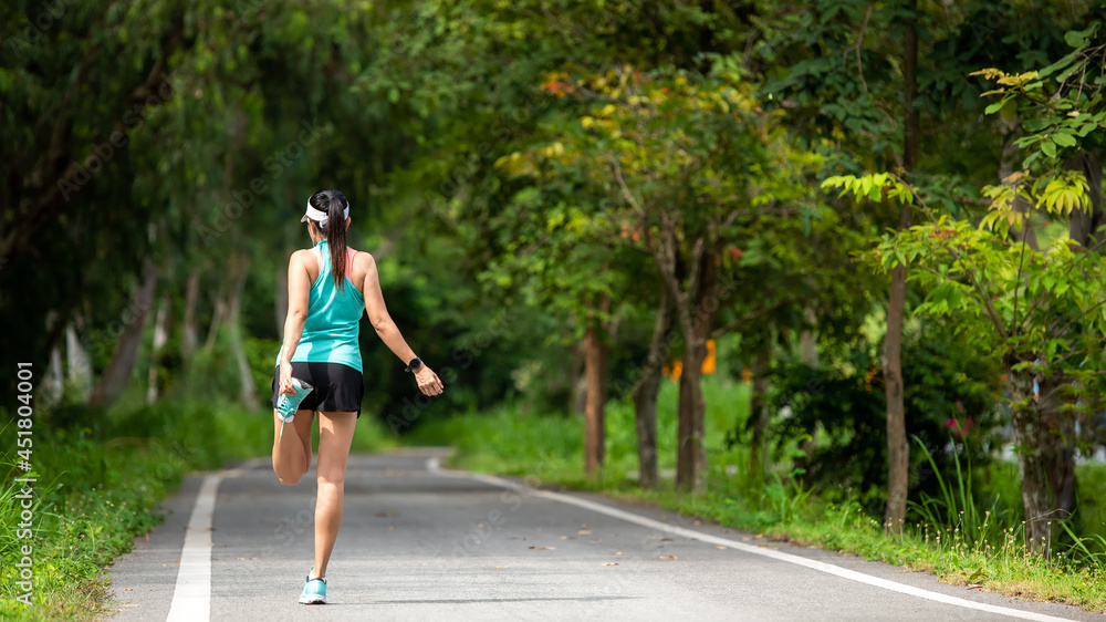 Healthy woman warming up before jogging run and relax stretching her arms and looking away in the road outdoor. Asian runner people workout fitness session, nature park background