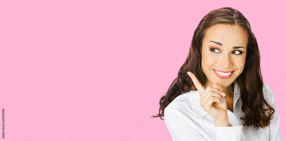 Young happy smiling woman in white confident blouse, showing pointing at copy space for text or imaginary. Business ad concept. Rose pink color background. Brunette businesswoman. Wide. Young happy smiling woman in white confident blouse, showing pointing at copy space for text or imaginary. Business ad concept. Rose pink color background. Brunette businesswoman. Wide.