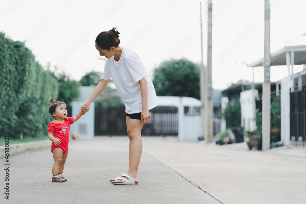 baby step in outdoor to practice balance walk in development according to the age of the child with mother helping daughter support