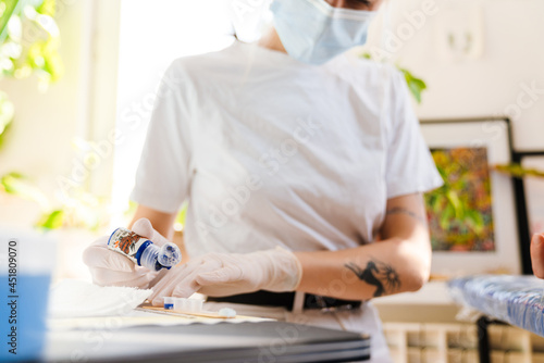 Young white tattoo artist in face mask working with ink at workshop