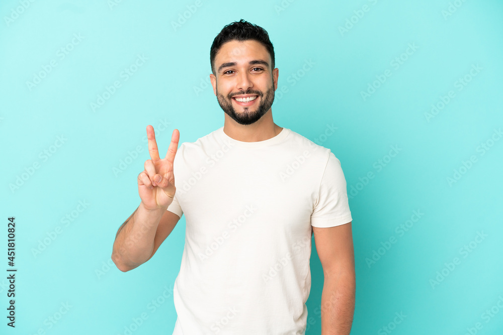 Young arab man isolated on blue background smiling and showing victory sign Young arab man isolated on blue background smiling and showing victory sign